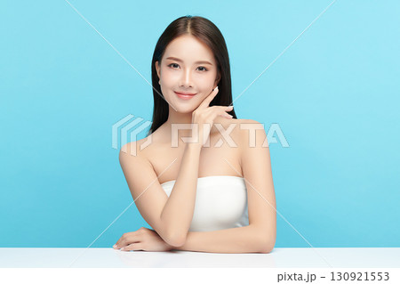 A beautiful young Asian woman with clean, fresh skin against a blue background. Skincare, facial treatment, cosmetology, beauty, and spa. An elegant portrait of an Asian woman. 130921553