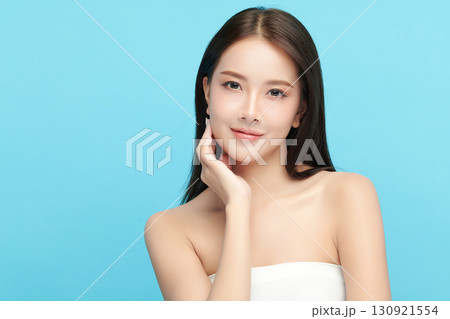 A beautiful young Asian woman with clean, fresh skin against a blue background. Skincare, facial treatment, cosmetology, beauty, and spa. An elegant portrait of an Asian woman. 130921554