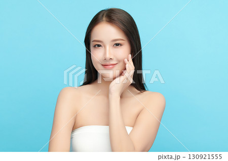 A beautiful young Asian woman with clean, fresh skin against a blue background. Skincare, facial treatment, cosmetology, beauty, and spa. An elegant portrait of an Asian woman. 130921555