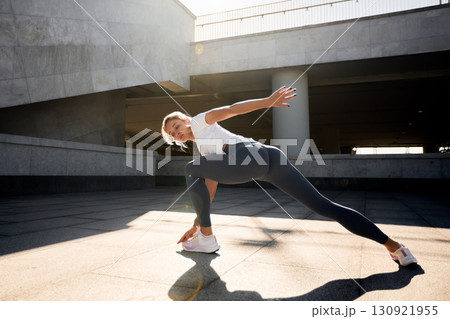 Woman stretching outdoors in urban space during a sunny day 130921955