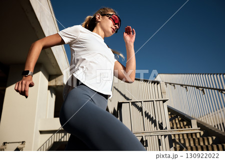 Woman jogging on stairs outdoors in sunlight wearing sportswear and sunglasses Woman jogging on stairs outdoors in sunlight wearing sportswear and sunglasses 130922022
