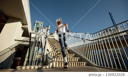 Female Athlete Running Upstairs in Urban Scenery During Morning Workout Female Athlete Running Upstairs in Urban Scenery During Morning Workout 130922026
