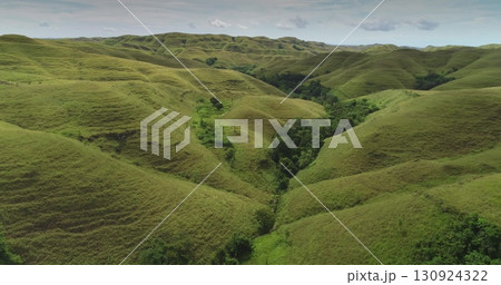 Rolling green hills stretch as far as the eye can see across Sumba island, Indonesia, captured in a breathtaking aerial view showcasing the untouched beauty of nature 130924322
