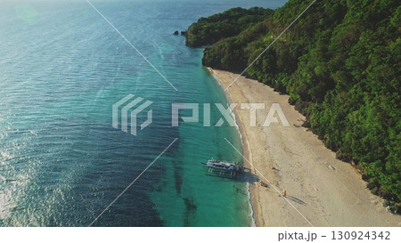 Tropical white sand beach and turquoise water meeting green rainforest in aerial drone view with banca boat on the shore and some tourists enjoying their vacation 130924342