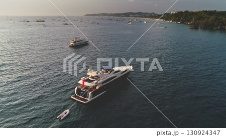 Aerial view of a luxury yacht sailing in the turquoise waters of Cagban Beach, Boracay Island, Philippines, surrounded by other boats and the coastline in the background, during a beautiful sunset 130924347