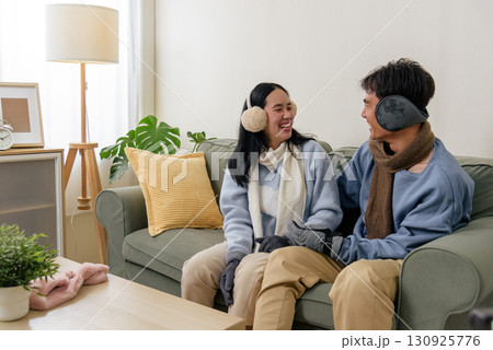 Winter day couple enjoy cozy home indoor leisure, happy people wear warm clothing including earmuffs scarves and gloves, smiling and relaxing together during cold winter, comfortable setting. Winter day couple enjoy cozy home indoor leisure, happy people wear warm clothing including earmuffs scarves and gloves, smiling and relaxing together during cold winter, comfortable setting. 130925776