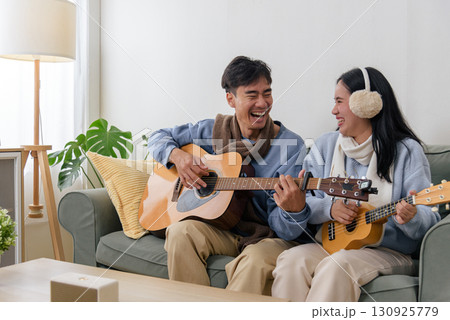 Winter, happy couple, family enjoying indoor home leisure, people playing acoustic guitar ukulele during cold winter day, bonding through music. 130925779