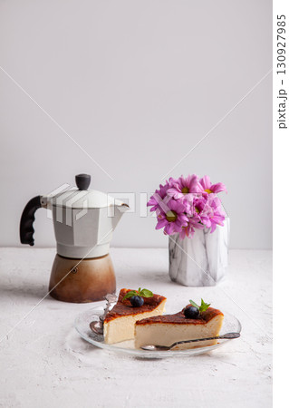 Slices of homemade Basque burnt cheesecake with blueberries and mint leaves, geyser coffee maker, flowers in a vase 130927985