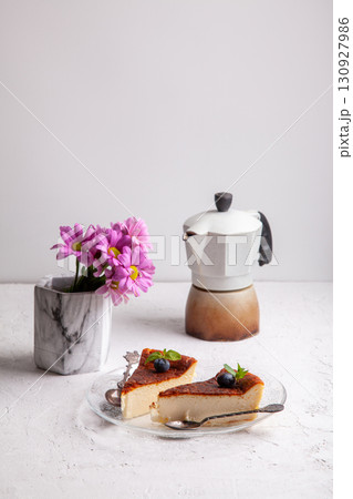 Slices of homemade Basque burnt cheesecake with blueberries and mint leaves, geyser coffee maker, flowers in a vase Slices of homemade Basque burnt cheesecake with blueberries and mint leaves, geyser coffee maker, flowers in a vase 130927986