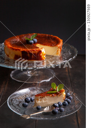 Homemade Basque burnt cheesecake with cream cheese, eggs and cream baked in a crumb crust. A slice of cheesecake on a plate with blueberries and mint leaves on dark background 130927989