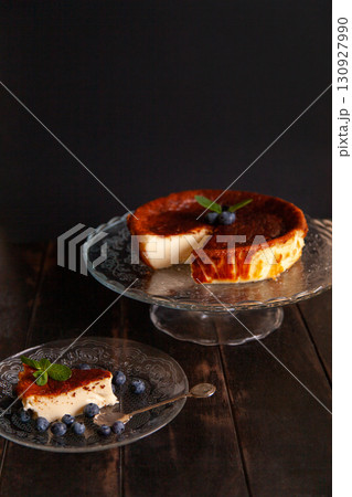Homemade Basque burnt cheesecake with cream cheese, eggs and cream baked in a crumb crust. A slice of cheesecake on a plate with blueberries and mint leaves on dark background Homemade Basque burnt cheesecake with cream cheese, eggs and cream baked in a crumb crust. A slice of cheesecake on a plate with blueberries and mint leaves on dark background 130927990