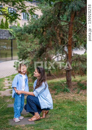 Mother and daughter wearing matching striped shirts and jeans while spending time together outdoors. Concept of family bonding, fashion harmony and casual everyday moments. Mother and daughter wearing matching striped shirts and jeans while spending time together outdoors. Concept of family bonding, fashion harmony and casual everyday moments. 130928258