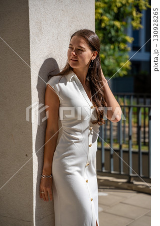 Young woman wearing a white midi dress walking outdoors in Old Money style. Concept of timeless fashion, graceful femininity and understated elegance in modern lifestyle. 130928265