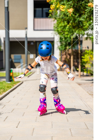 Little girl learning to roller skate for the first time at the age of five. Concept of physical development, balance training and childhood independence through active play. Little girl learning to roller skate for the first time at the age of five. Concept of physical development, balance training and childhood independence through active play. 130928279