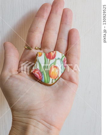 HumClose-up of a human hand holding a bitten heart-shaped gingerbread cookie. Sweet dessert and holiday treat concept.an hand holding gingerbread heart cookie. High quality photo 130929525