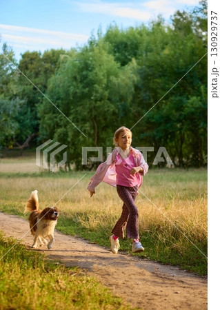 Girl running joyfully with dog along forest path in warm light Girl running joyfully with dog along forest path in warm light 130929737