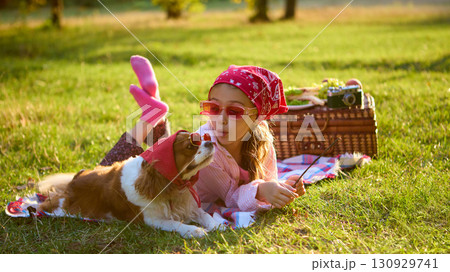 Girl in red bandana lying on blanket with dog in sunglasses enjoying picnic Girl in red bandana lying on blanket with dog in sunglasses enjoying picnic 130929741