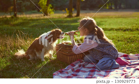 Girl feeding sandwich to dog on blanket in sunny meadow Girl feeding sandwich to dog on blanket in sunny meadow 130929773