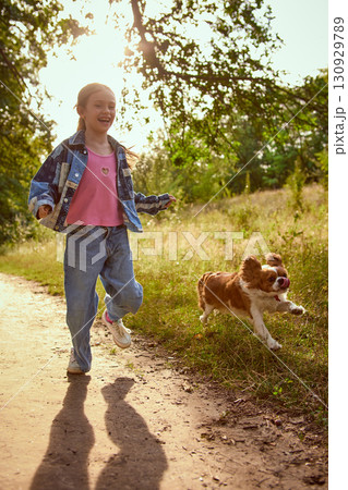 Girl laughing while running with dog in meadow under sunlight 130929789