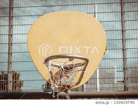 an oval-shaped wooden backboard, a metal hoop ring and a white net, all positioned against a wire fence in the background at outdoor basketball courts 130929798