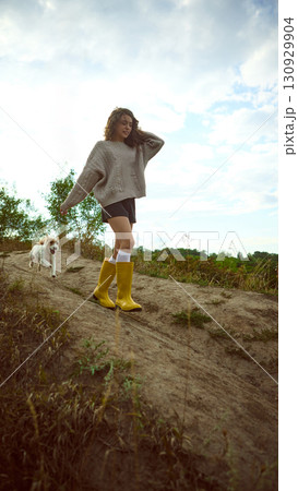 Woman walking downhill with dog in countryside wearing yellow boots Woman walking downhill with dog in countryside wearing yellow boots 130929904