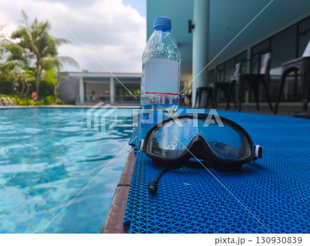 Plastic water bottle and wet swimming goggles on poolside mat, symbolizing summer recreation, hydration, and swimming activities. Plastic water bottle and wet swimming goggles on poolside mat, symbolizing summer recreation, hydration, and swimming activities. 130930839
