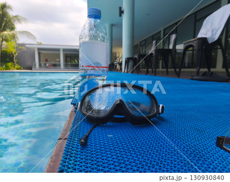 Plastic water bottle and wet swimming goggles on poolside mat, symbolizing summer recreation, hydration, and swimming activities. Plastic water bottle and wet swimming goggles on poolside mat, symbolizing summer recreation, hydration, and swimming activities. 130930840