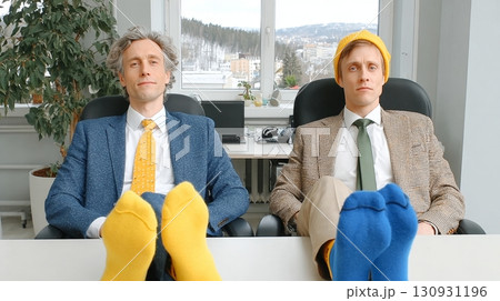 Two coworkers sit in an office, showing off their bright socks for odd socks day aimed at combating bullying 130931196