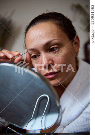Woman Trimming Eyebrows With Tweezers in Brightly Lit Room 130931362