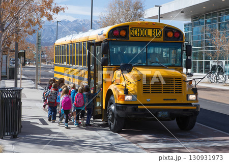A group of elementary school children board a yellow school bus. A group of elementary school children board a yellow school bus. 130931973