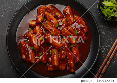 Traditional Korean tteokbokki served on black plate with chopsticks and sesame seeds on black rustic background 130932214