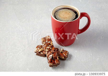 red cup of hot coffee and two nut caramel bars on a gray stone table 130933975
