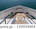 View from the bow deck of a modern luxury yacht with teak wood flooring, stainless steel railings, and nautical ropes. The yacht is sailing on calm blue sea, symbolizing travel, marine lifestyle, and 130934004