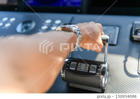 A close up view of a yacht or ship bridge with a captains hand operating the throttle controls. 130934006