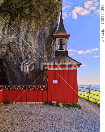 Scenic chapel near rocky cliff with bell tower and cross under clear blue sky 130934396