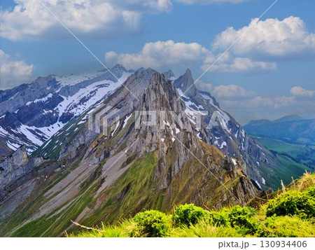 Majestic mountain range with snow-capped peaks and lush green meadows under a clear blue sky in summer 130934406