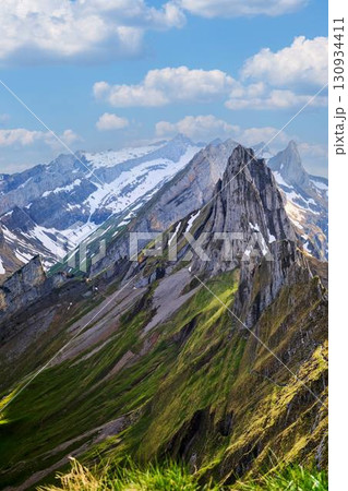 Majestic mountain landscape showcasing rugged peaks and lush green valleys under a blue sky Majestic mountain landscape showcasing rugged peaks and lush green valleys under a blue sky 130934411