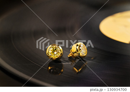Two gold earrings are on a black record 130934700