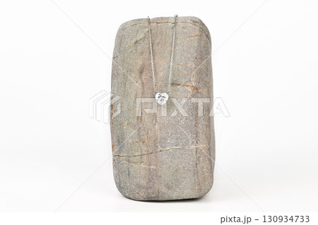 A silver necklace with a heart shaped pendant is displayed on a gray stone A silver necklace with a heart shaped pendant is displayed on a gray stone 130934733