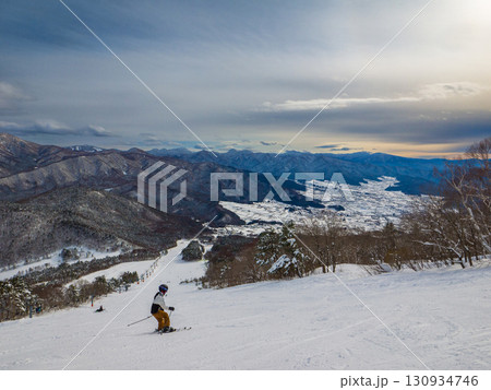 雪山を望む雄大な景色の中を滑走する一人のスキーヤー (長野県、山ノ内町、夜間瀬) 130934746