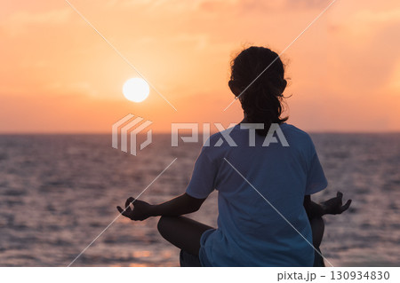Young woman meditate at sunset over the sea. 130934830