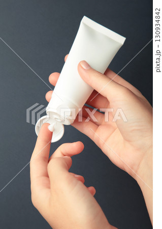 Hand holding blank white plastic tube on dark blue background. Vertical photo 130934842