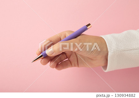 Young woman holding purple pen on pink background. 130934882