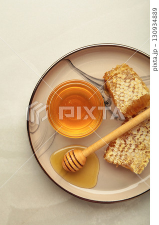 Bowl of sweet honey, dippers and combs on plate on light background. Vertical photo 130934889