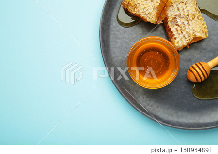 Bowl of sweet honey, dippers and combs on dark plate on blue background 130934891