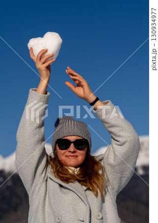 Snow Heart Winter Mountains: Woman playfully displays a heart-shaped snowball outdoors in a snowy mountain range during winter. Snow Heart Winter Mountains: Woman playfully displays a heart-shaped snowball outdoors in a snowy mountain range during winter. 130934977
