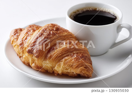 A steaming cup of coffee next to a butter croissant 130935030