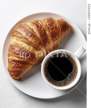 A steaming cup of coffee next to a butter croissant 130935032