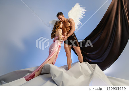 Couple posing as angel and goddess against a stylistic backdrop Couple posing as angel and goddess against a stylistic backdrop 130935439