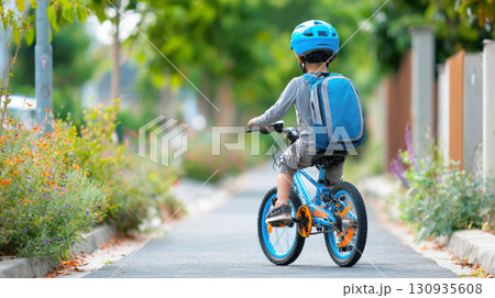 A young boy wearing a backpack and protective helmet is seen from behind as he rides his bicycle on suburban sidewalk. Image captures a moment of active, safe, independent travel on his way to school A young boy wearing a backpack and protective helmet is seen from behind as he rides his bicycle on suburban sidewalk. Image captures a moment of active, safe, independent travel on his way to school 130935608